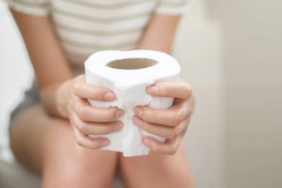 Person holding a roll of toilet paper while sitting.