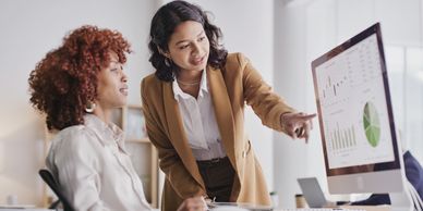 Two women analyzing charts on a computer screen in an office.