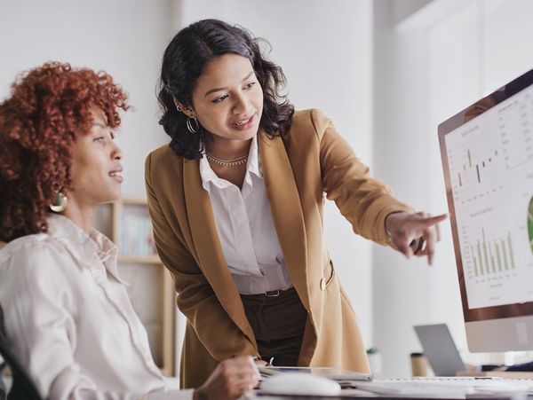 Two professional women discussing data on a computer screen in an office.
