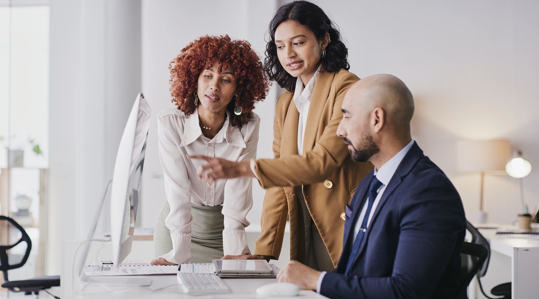 Three colleagues discussing work at a computer in an office.