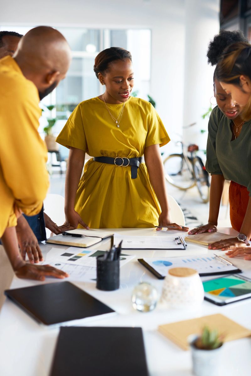 Black woman brainstorming with paperwork, teamwork and planning collaboration strategy in agency. Group of designers meeting with documents, business information feedback and graphs of data analysis