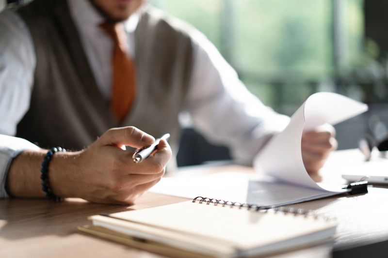 Businessman hands holding pen for working with stack of paper files, searching information, business report papers and piles of unfinished documents in modern office