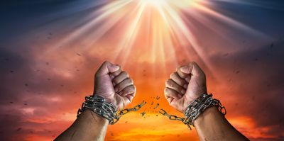Hands breaking free from chains against a dramatic sunset and radiant light.
