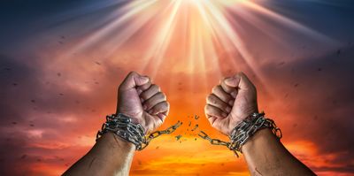 Hands breaking free from chains against a dramatic sunset and radiant light.
