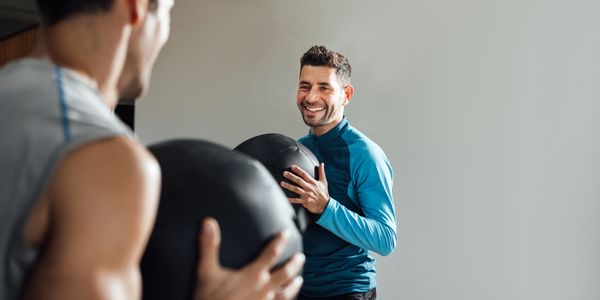 Two men holding medicine balls and smiling during a workout.