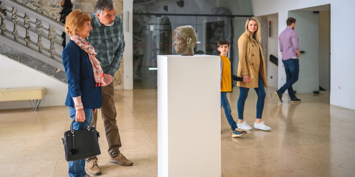 People observing a sculpture head displayed on a pedestal in a museum.