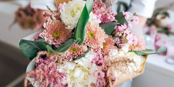 A bouquet of pastel-colored flowers wrapped in brown paper.