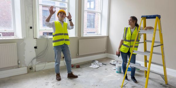 Two construction workers discussing inside a room under renovation.