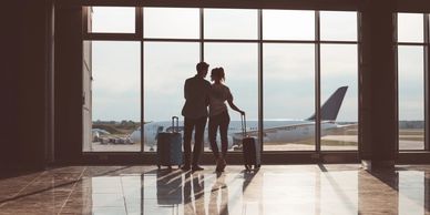 Couple with luggage at airport terminal window.