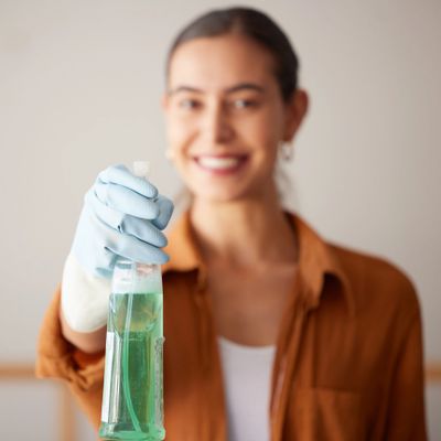 Smiling woman holding a spray bottle with cleaning solution wearing a glove.