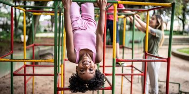Happy children playing on jungle gym at a park with adult supervision.