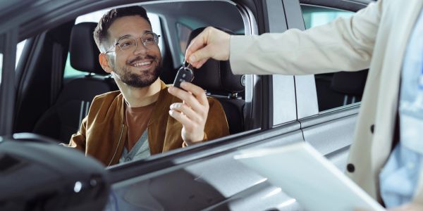 Man happily receiving car keys while sitting inside a car.