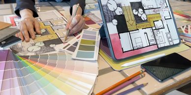Architect working on floor plans with color swatches and digital tablet.