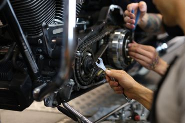 Hands working with tools on a motorcycle engine chain.