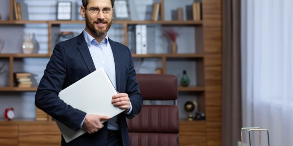 Man in suit holding a laptop in an office.