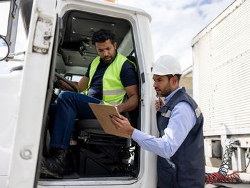 Two workers check documents in a truck cabin.