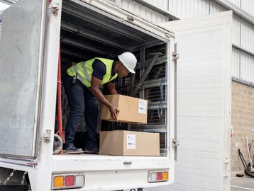 Worker unloading cardboard boxes from a delivery truck inside a warehouse.