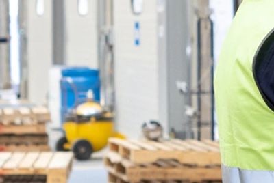Person wearing a high-visibility vest near wooden pallets in warehouse.