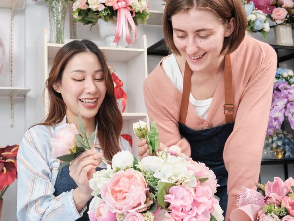 Two women happily arranging a bouquet of pink and white flowers.