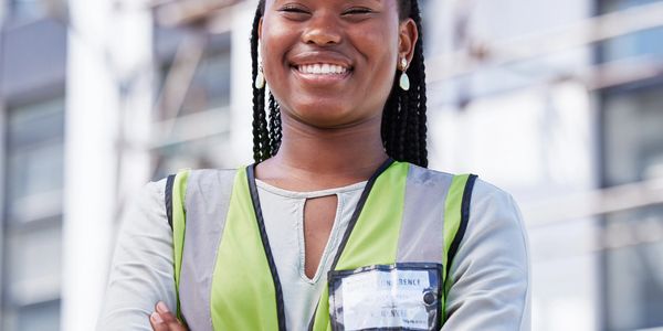 Confident female construction worker in safety gear smiling outdoors.