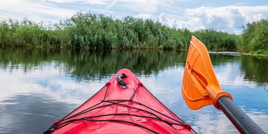 Paddling a red kayak on calm water surrounded by green reeds.