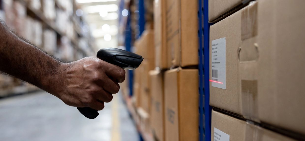 Hand scanning barcode on box in warehouse with scanner.