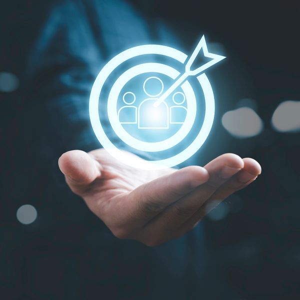 Hand holding a glowing target with a dart hitting the center, symbolizing customer targeting.