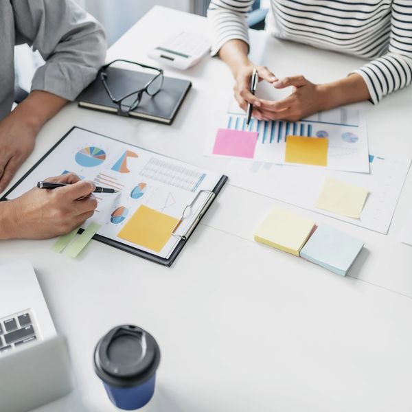 Two people discussing charts at a desk with sticky notes.