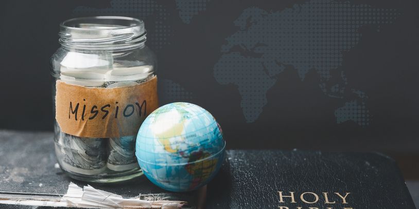 Jar labeled 'Mission' with money, a small globe, and a Holy Bible.