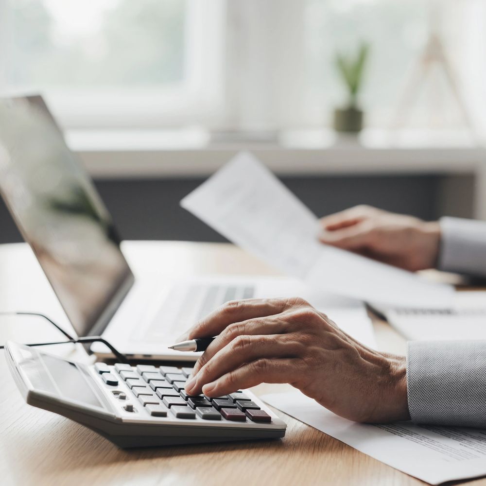 Person using calculator and laptop to review documents at a desk.