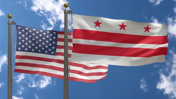 Two flags, the United States and Washington D.C., waving against a blue sky.