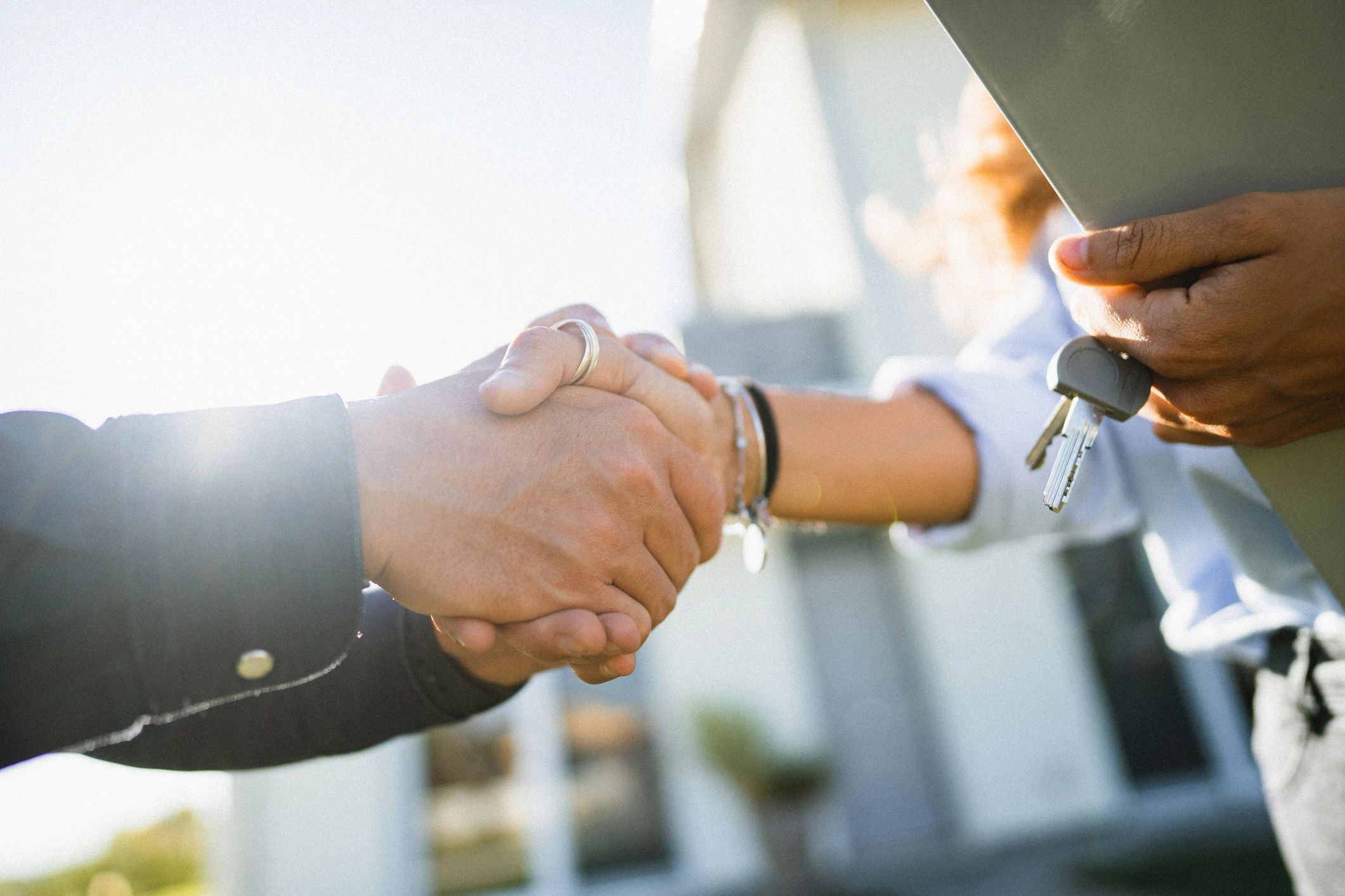 Two people shaking hands, one holding house keys and a laptop.