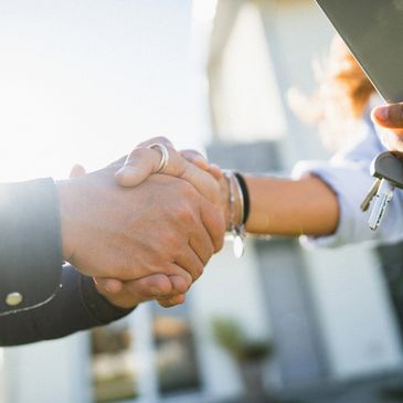 Handshake with house keys in hand outside a home.