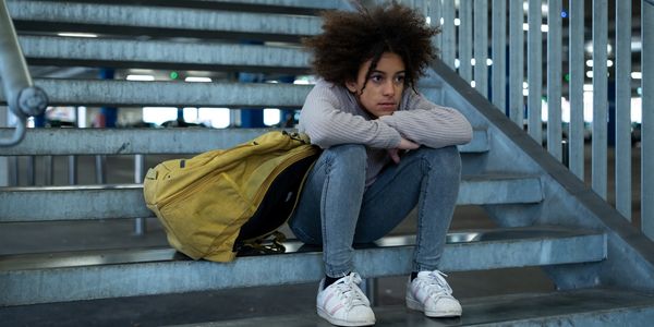 Teen girl sitting pensively on metal stairs with a yellow backpack.
