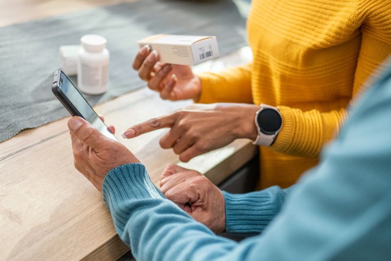Mid section of mature couple using mobile while holding medicine box.