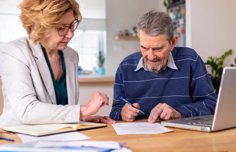 Mature woman helping senior man, 91 years old, with paperwork. He signing documents