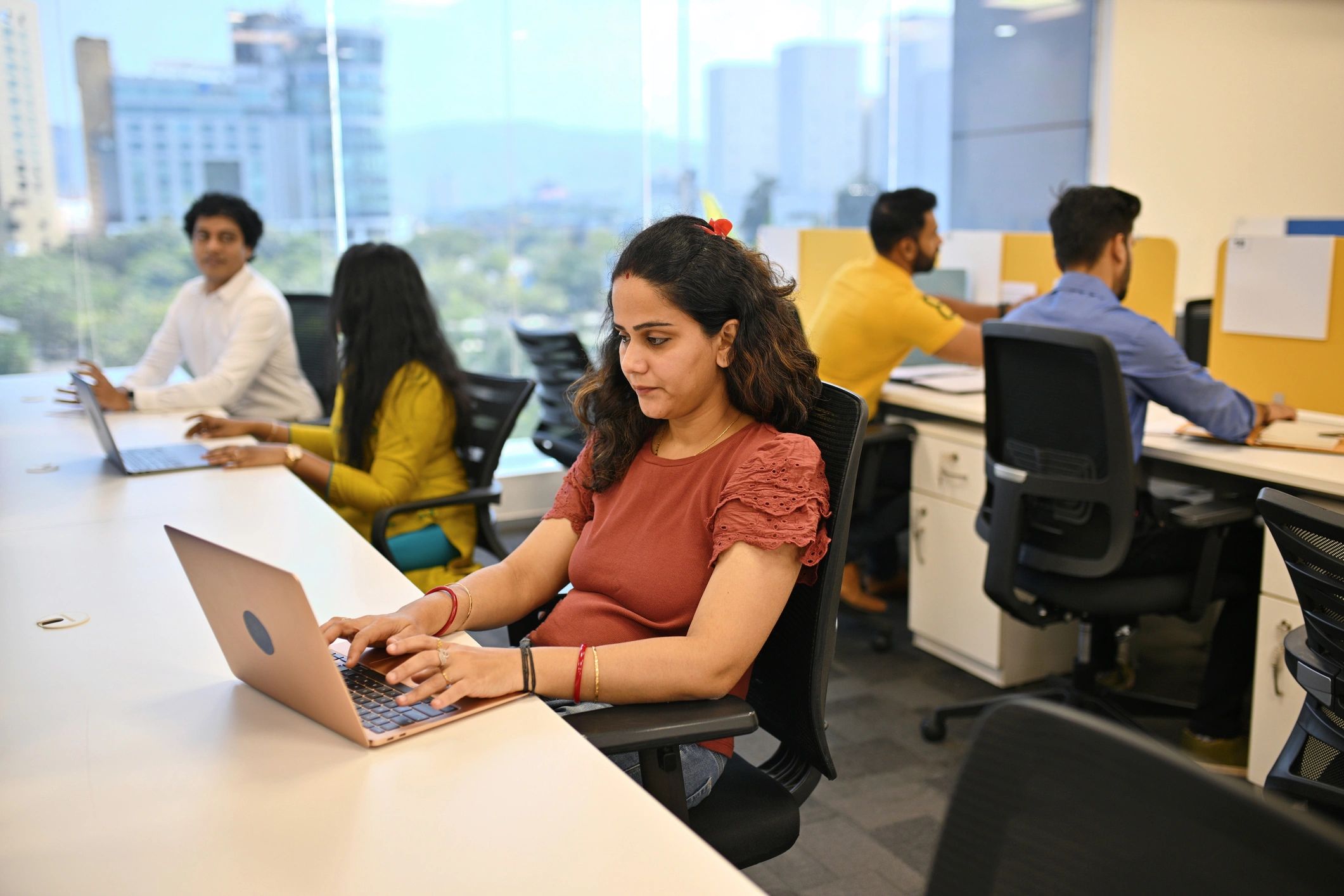 People working on laptops in a modern office with large windows.