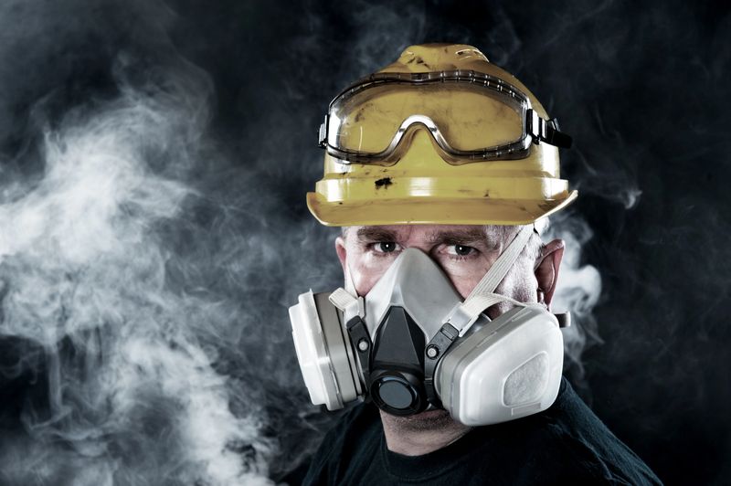 A rescue worker wears a respirator in a smokey, toxic atmosphere.  Image show the importance of protection readiness and safety.