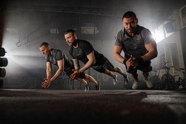 Three men perform push-up exercises mid-air in a gym.