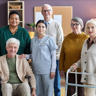 A group of elderly people and a nurse smiling together indoors.