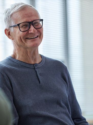 Smiling elderly man wearing glasses in a casual setting.
