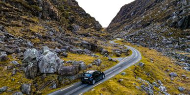 A car driving on a winding mountain road surrounded by rocky terrain.