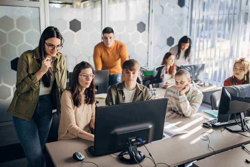 Group of male and female students using desktop computer on class in programming school.