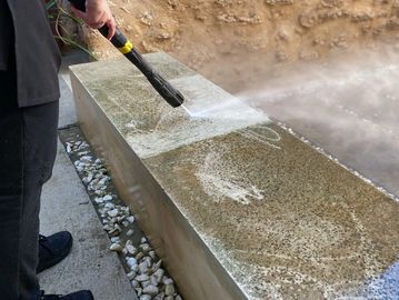 Person cleaning a dirty concrete bench with a pressure washer.
