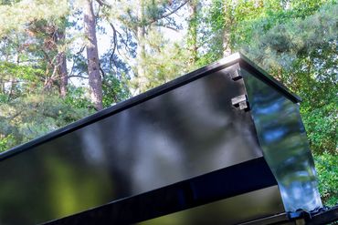 Black dump trailer tilted for unloading in a wooded area.