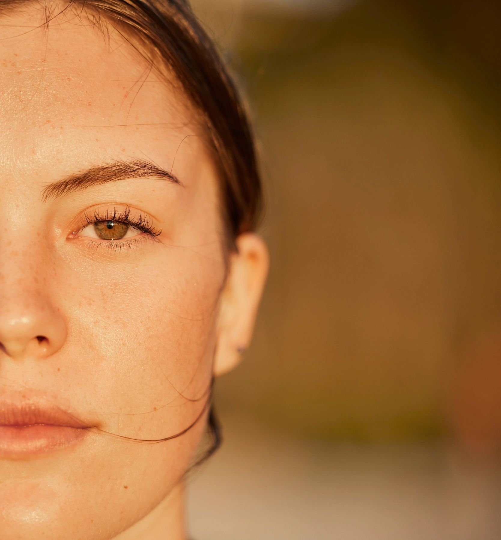 Close-up of a woman's eye and freckles in warm light.