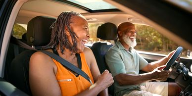 Two older adults happily driving in a car.