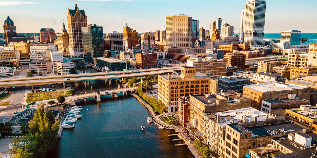 A vibrant city skyline along a river with boats and bridges under a blue sky.