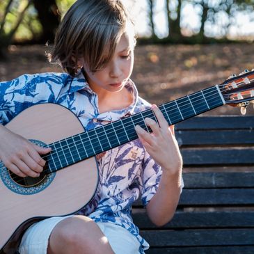 Child sitting on a park bench playing a beginner guitar