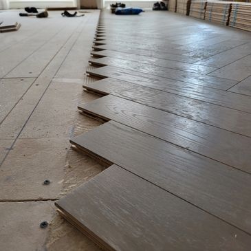 Wooden floorboards being installed in a staggered pattern.